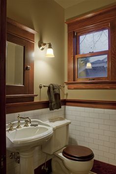 a white toilet sitting next to a sink in a bathroom under a window with wooden trim