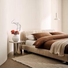 a bed sitting in a bedroom next to a vase with flowers on top of it