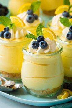 small desserts with lemon and blueberries in glass jars on a white plate next to spoons