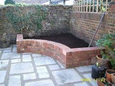 a brick wall and garden area with potted plants in the corner, next to a fence