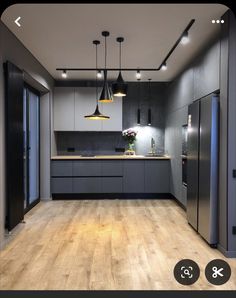 an empty kitchen with wooden floors and black cabinets in the center, surrounded by hanging lights