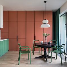 a dining room with green chairs and a black table in front of an orange wall