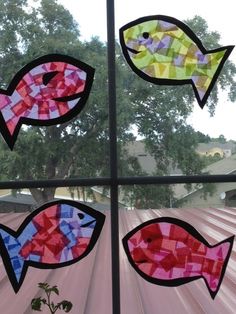 four different colored fish are shown through a window pane with trees in the background