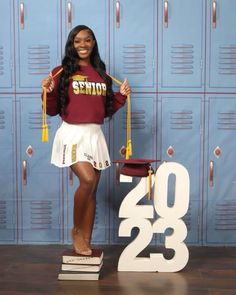 a woman standing in front of lockers holding a graduation cap and tassle