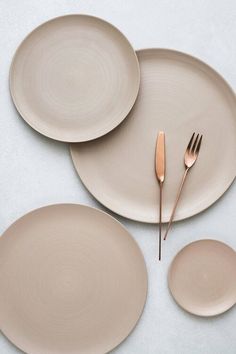 three plates and two spoons are arranged on a white surface with one fork in the middle