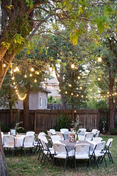 an outdoor table and chairs are set up under the trees with lights strung from them