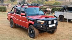 a red four door pick up truck parked next to a white pickup truck in a field