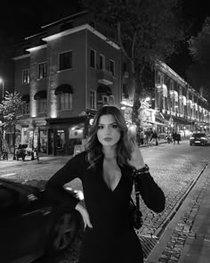 a woman standing on the side of a road in front of a building at night