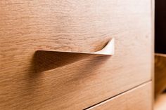 a close up view of a drawer handle on a wooden cabinet with light wood grained finish