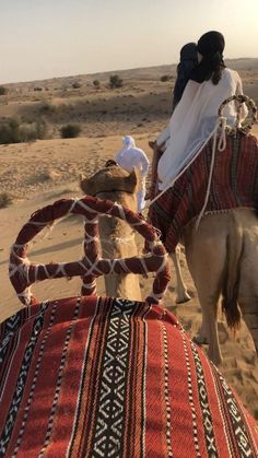 a man and woman riding on the back of a camel in the desert with their backs to each other