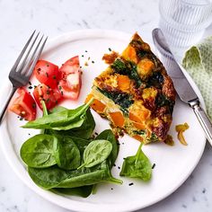 a plate with spinach, tomato and quiche on it next to a fork