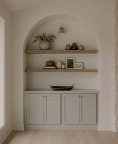 a white room with shelves and vases on top of it, along with pictures