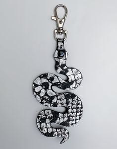 a snake keychain hanging from a hook on a white surface with black and white designs