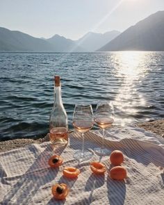 two wine glasses and three donuts sit on a towel near the water with mountains in the background