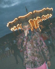 a man standing in front of a merry go round at night with his cell phone to his ear