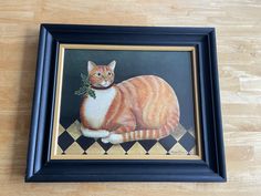 an orange and white cat sitting on top of a wooden floor next to a framed painting