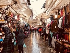 people are walking through an open market with umbrellas over their heads and clothes hanging from the ceiling