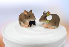 two figurines of mice sitting on top of a white cake covered in frosting