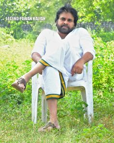 a man sitting on top of a white chair in the middle of some grass and trees