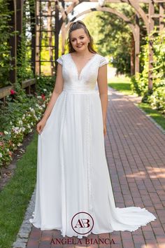 a woman wearing a white dress standing on a brick walkway in front of trees and flowers