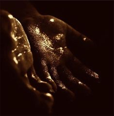 two hands are covered in gold dust and shines on the dark surface, with one hand holding another