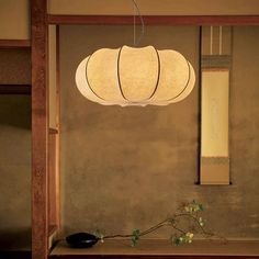 a lamp hanging from the ceiling above a table with flowers on it and a vase next to it