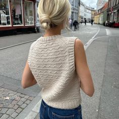 a woman walking down the street with her back turned to the camera, wearing jeans and a sweater