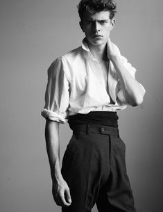 black and white photograph of man in dress shirt with hand on his chin, standing against wall