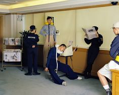 several people in uniforms are standing and sitting around while one man is reading a newspaper