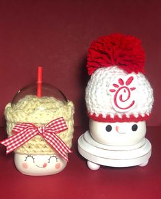 two knitted items sitting next to each other on a red surface with one wearing a hat and the other holding an apple