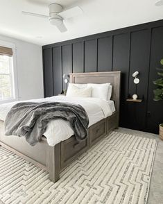 a bedroom with black paneled walls, white bedding and a rug on the floor