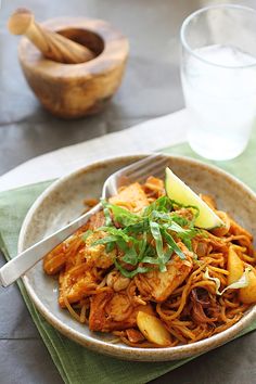 a bowl filled with noodles and meat on top of a green napkin next to a glass of water