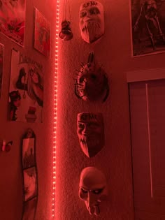 several masks are hanging on the wall with red light coming from behind them in a dark room