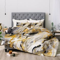 a bed with yellow and black marble print on the comforter, next to a plant