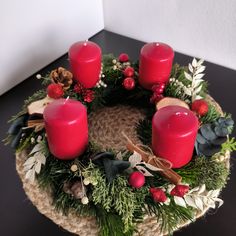 a christmas wreath with three red candles and evergreens on it, sitting on a table