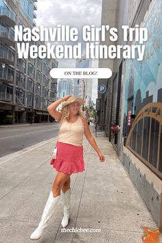 a woman in a pink dress and white cowboy boots is standing on the sidewalk with her arms behind her head