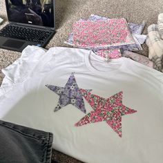 a laptop computer sitting on top of a bed next to three stars t - shirts