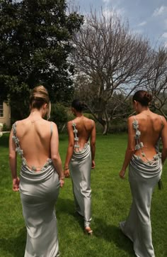 three women walking in the grass with their back to the camera, one wearing a white dress