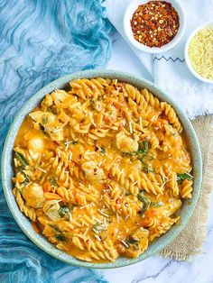 a bowl filled with pasta and sauce on top of a blue cloth next to two bowls