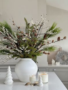 a white vase filled with lots of greenery on top of a table next to candles