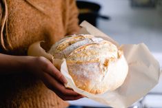 a person holding a loaf of bread in their hand and wrapped in wax paper on the other side