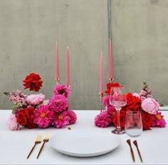 the table is set with pink and red flowers, candles, and wine glasses on it