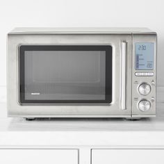 a silver microwave oven sitting on top of a white counter next to some cupboards