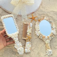 someone is holding three mirrors on the beach with seashells and starfish attached to them