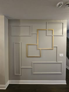 an empty room with white walls and gold frames on the wall, along with dark wood flooring