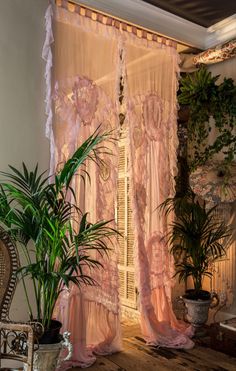 a living room filled with lots of plants next to a window covered in sheer curtains