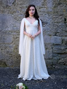 a woman in a white dress standing next to a stone wall and wearing a veil