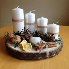 some white candles are sitting on a wood slice with pine cones and other decorations around it