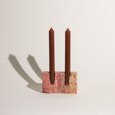 two candles sitting on top of each other in front of a white wall and shadow