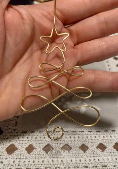 a hand holding a gold wire christmas tree ornament on top of a table